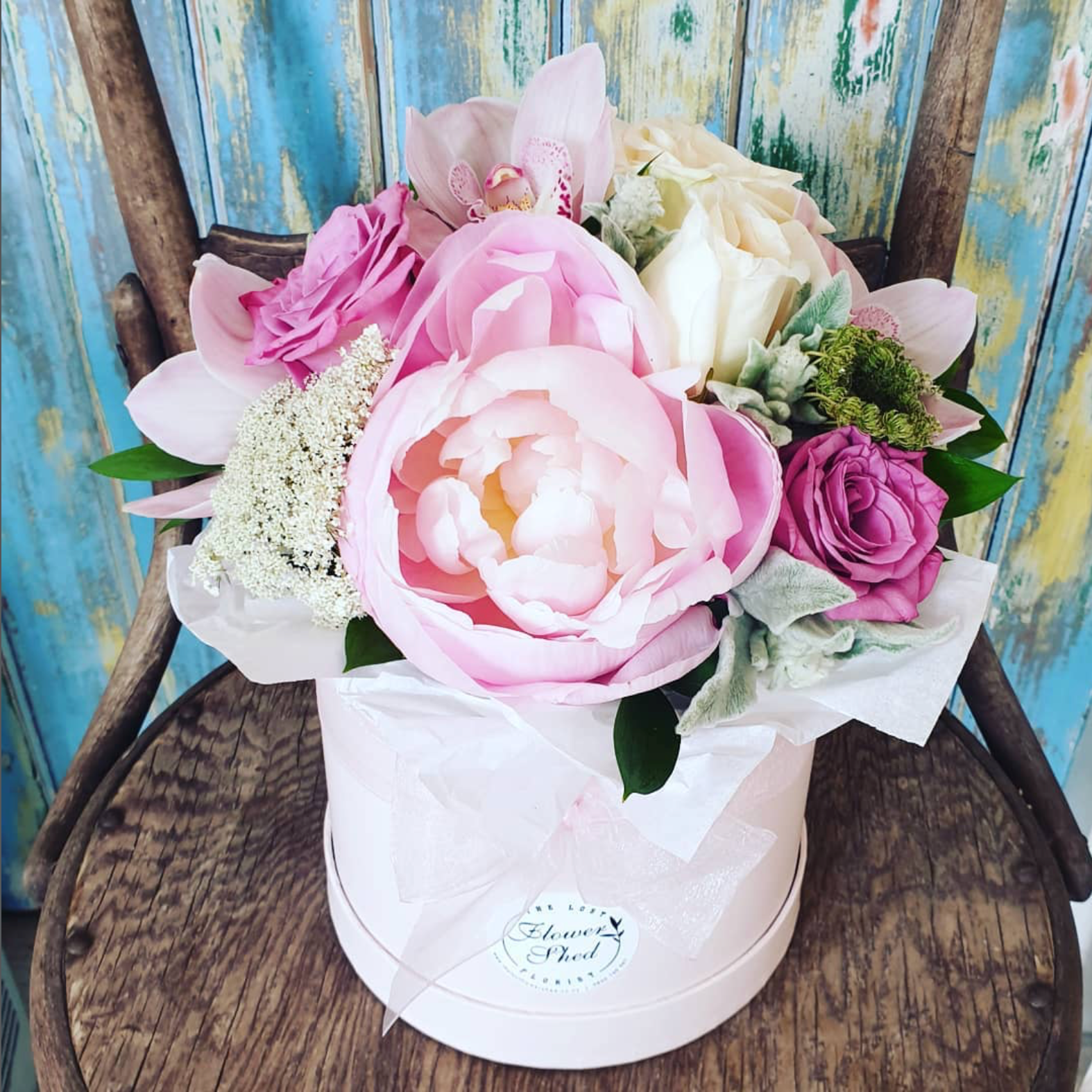 Bouquet of pink and white flowers in a white box on a wooden chair with a colorful background.