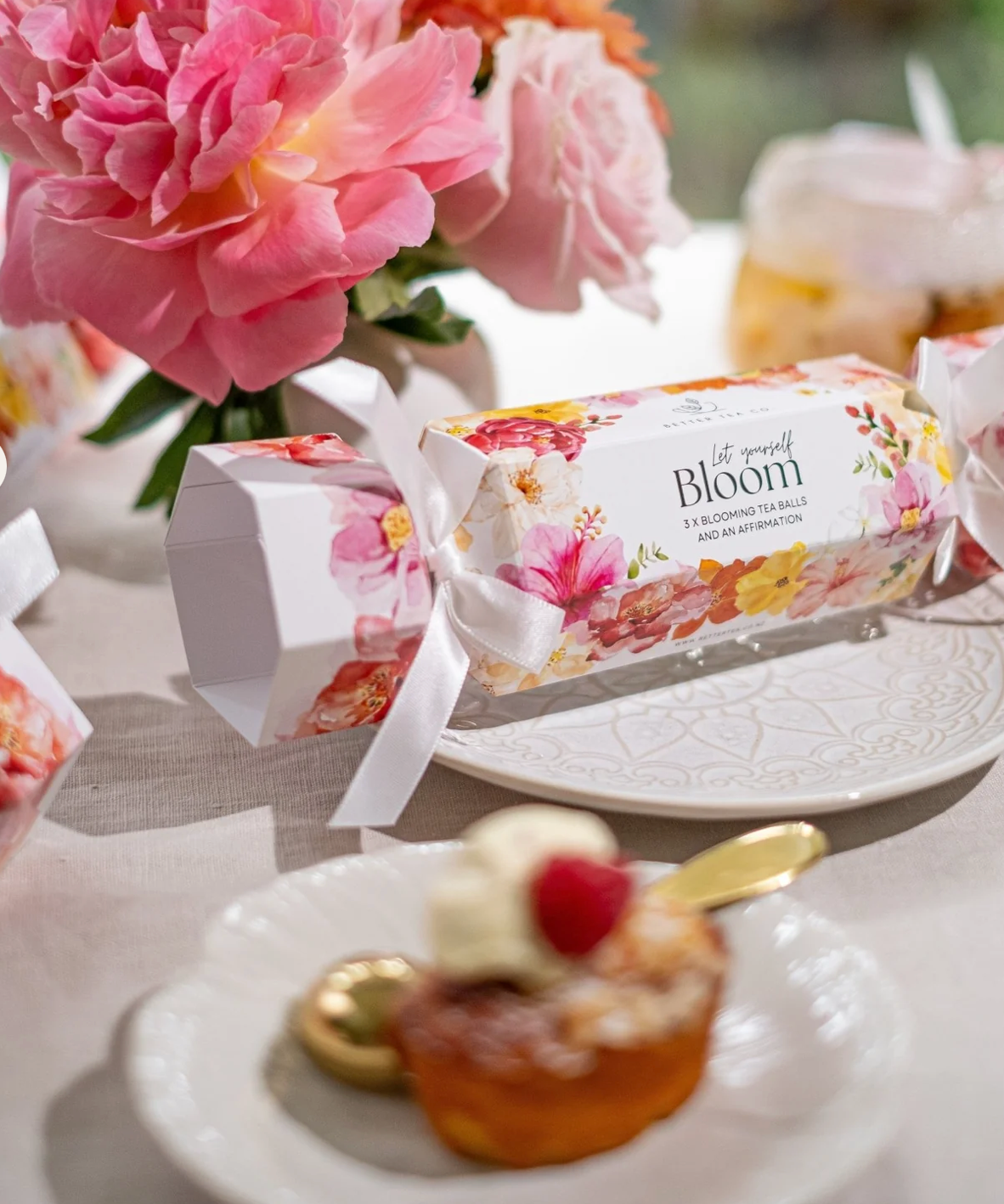 Floral-themed gift box on a table with a dessert and flowers in the background