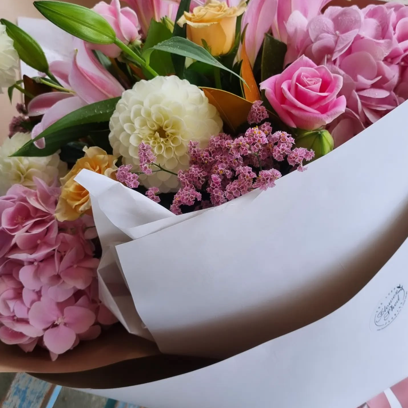 Bouquet of flowers wrapped in white paper with a visible brand logo.