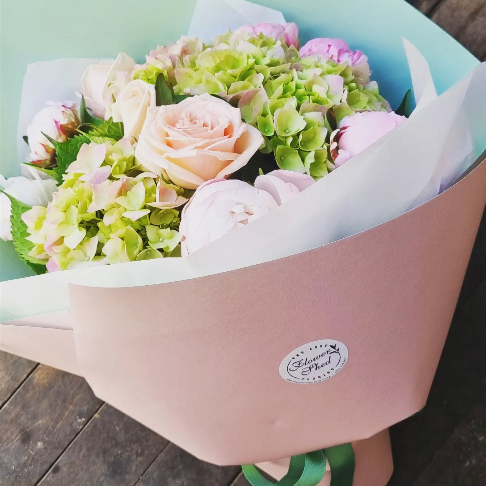 Bouquet of flowers in a pink box with a visible brand label on a wooden surface