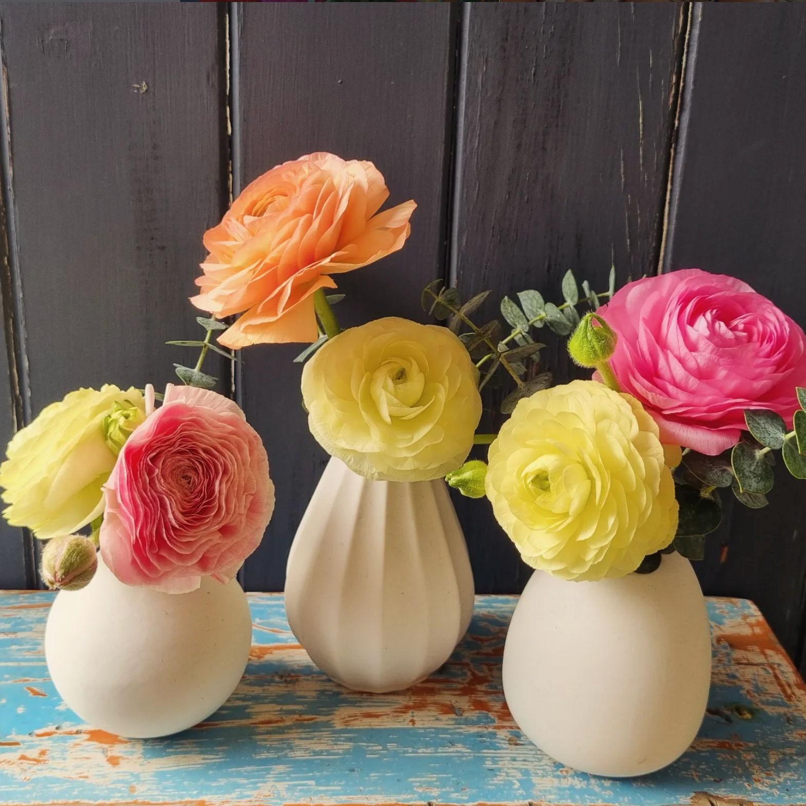Three white vases with colorful flowers on a rustic wooden surface.