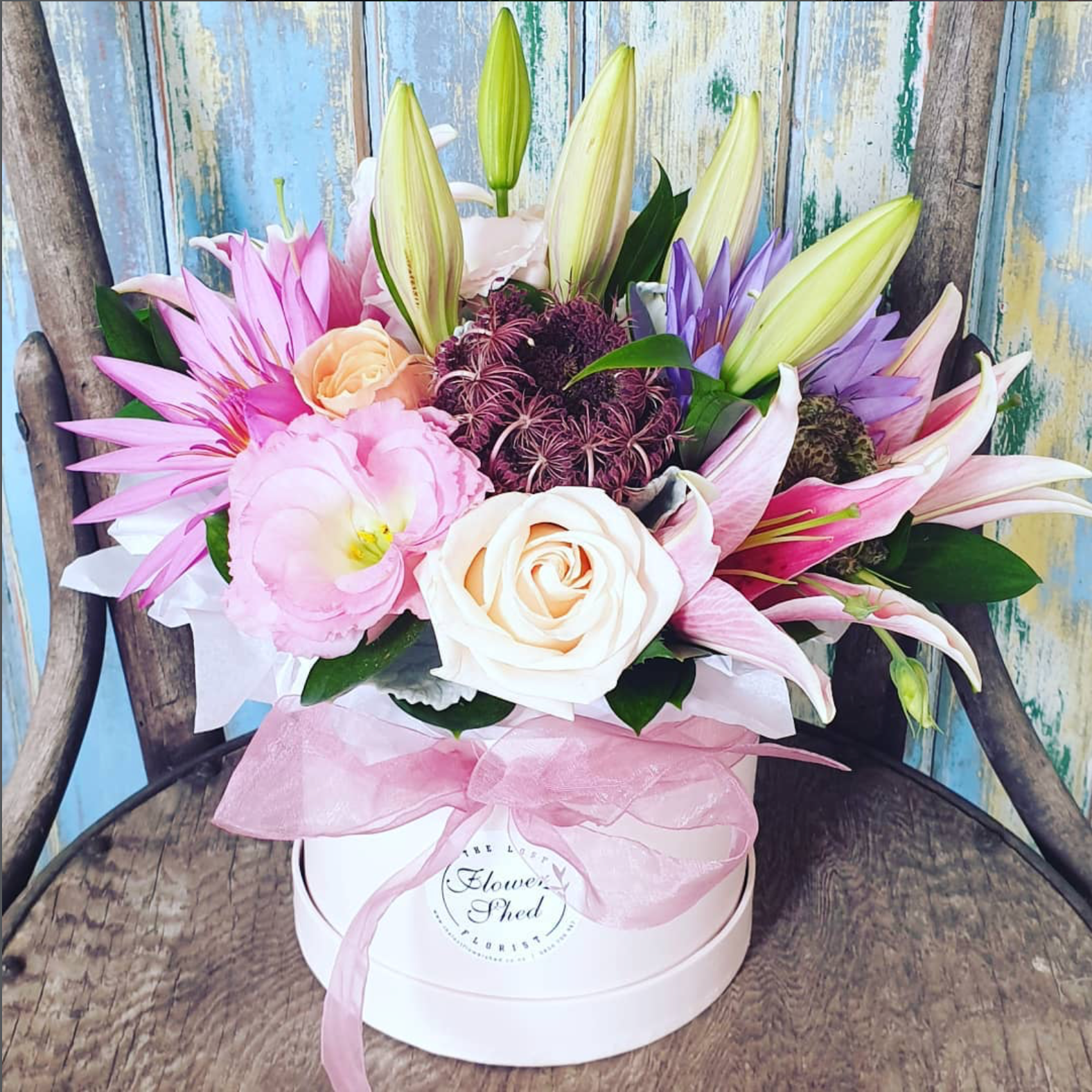 Floral arrangement in a white box with a pink bow on a wooden surface.