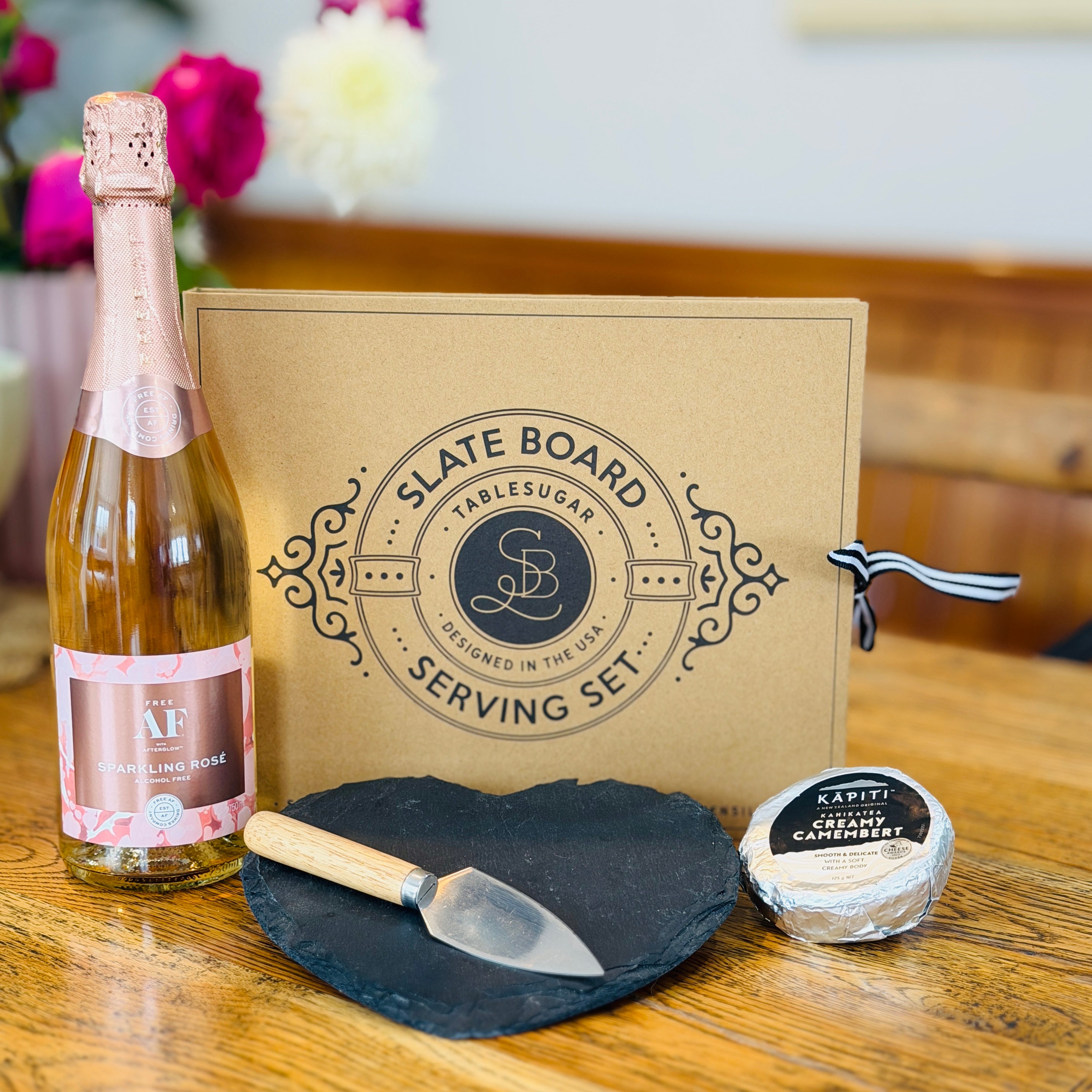 a bottle of AF Rosé, a heart-shaped slate cheese board with knife set, and a creamy Kapiti cheese,
