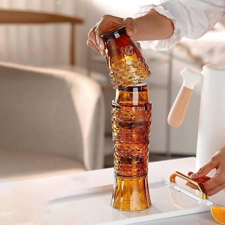 Person pouring a drink into a tall, cylindrical glass with a textured surface on a kitchen counter.