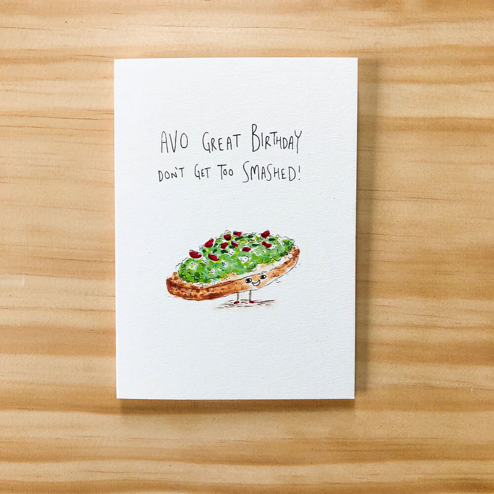 Greeting card with avocado toast illustration and humorous birthday message on a wooden surface
