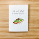 Greeting card with avocado toast illustration and humorous birthday message on a wooden surface
