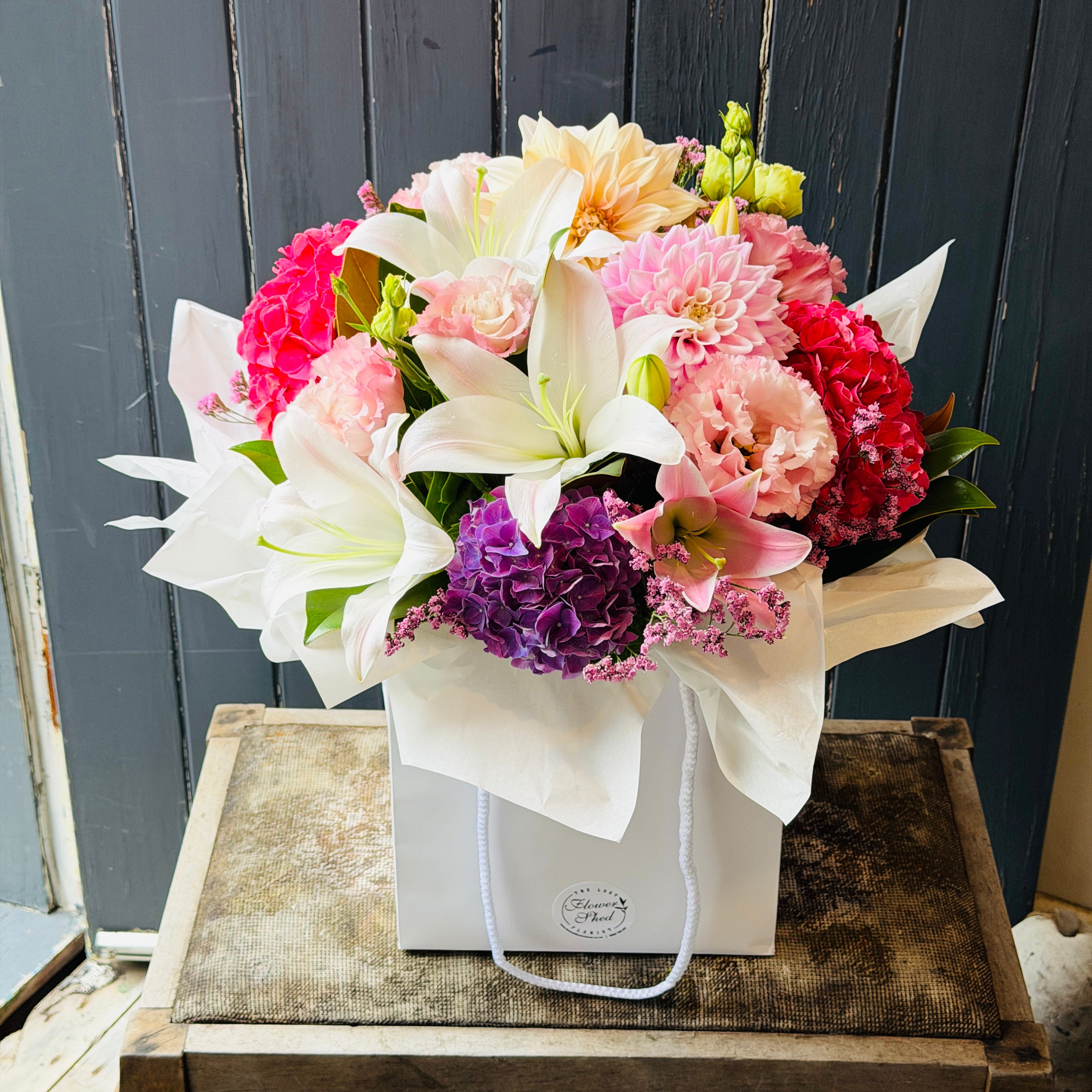 Bouquet posy of flowers in a white gift bag  on a wooden surface with a dark wooden background