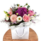 Bouquet posy of flowers in a white gift bag  on a wooden surface with a dark wooden background