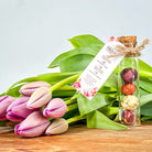 floral tea balls in a glass tube with a clear mug with a bloomed flower tea steeping in hot water on a bread board