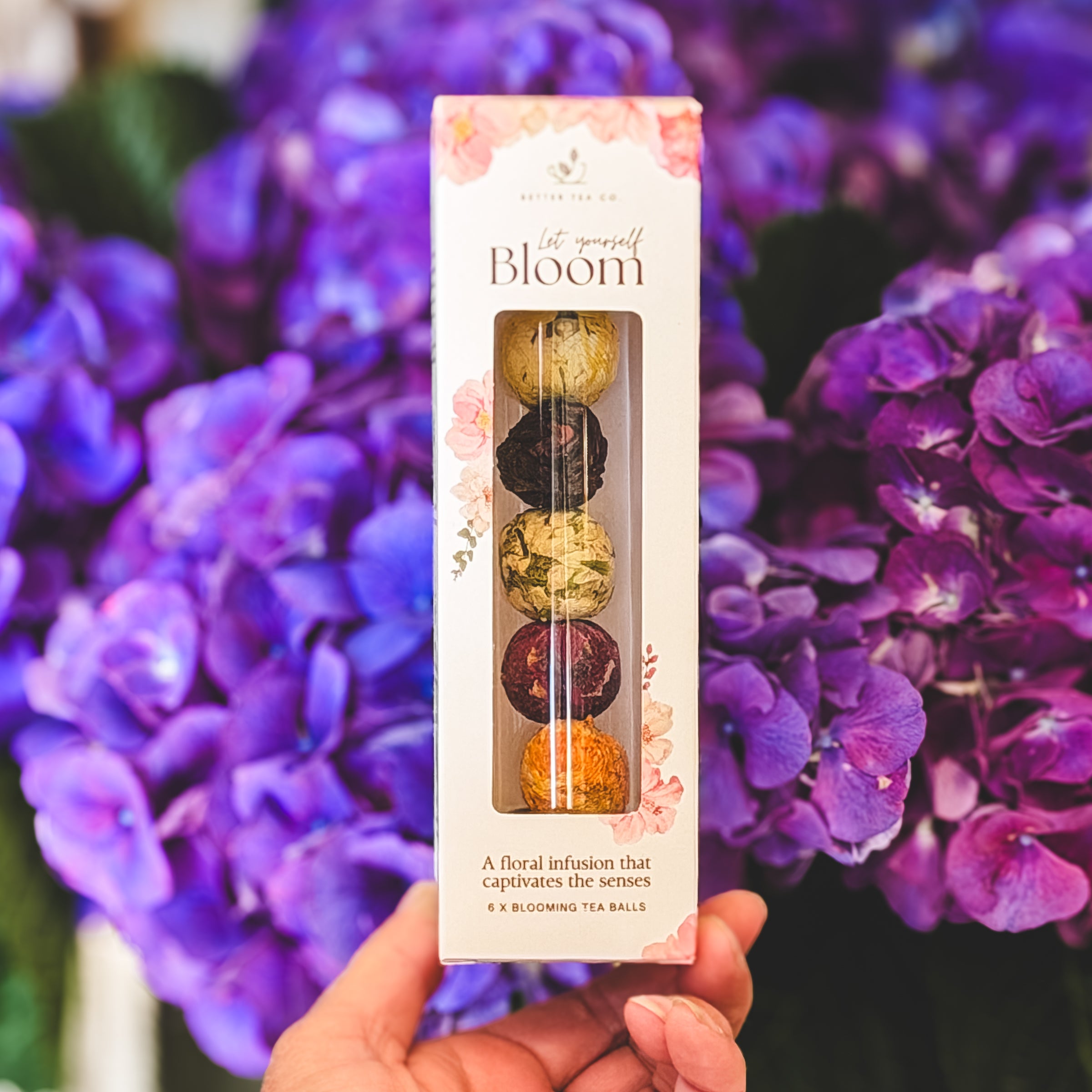 floral tea balls in a glass tube with a clear mug with a bloomed flower tea steeping in hot water on a bread board