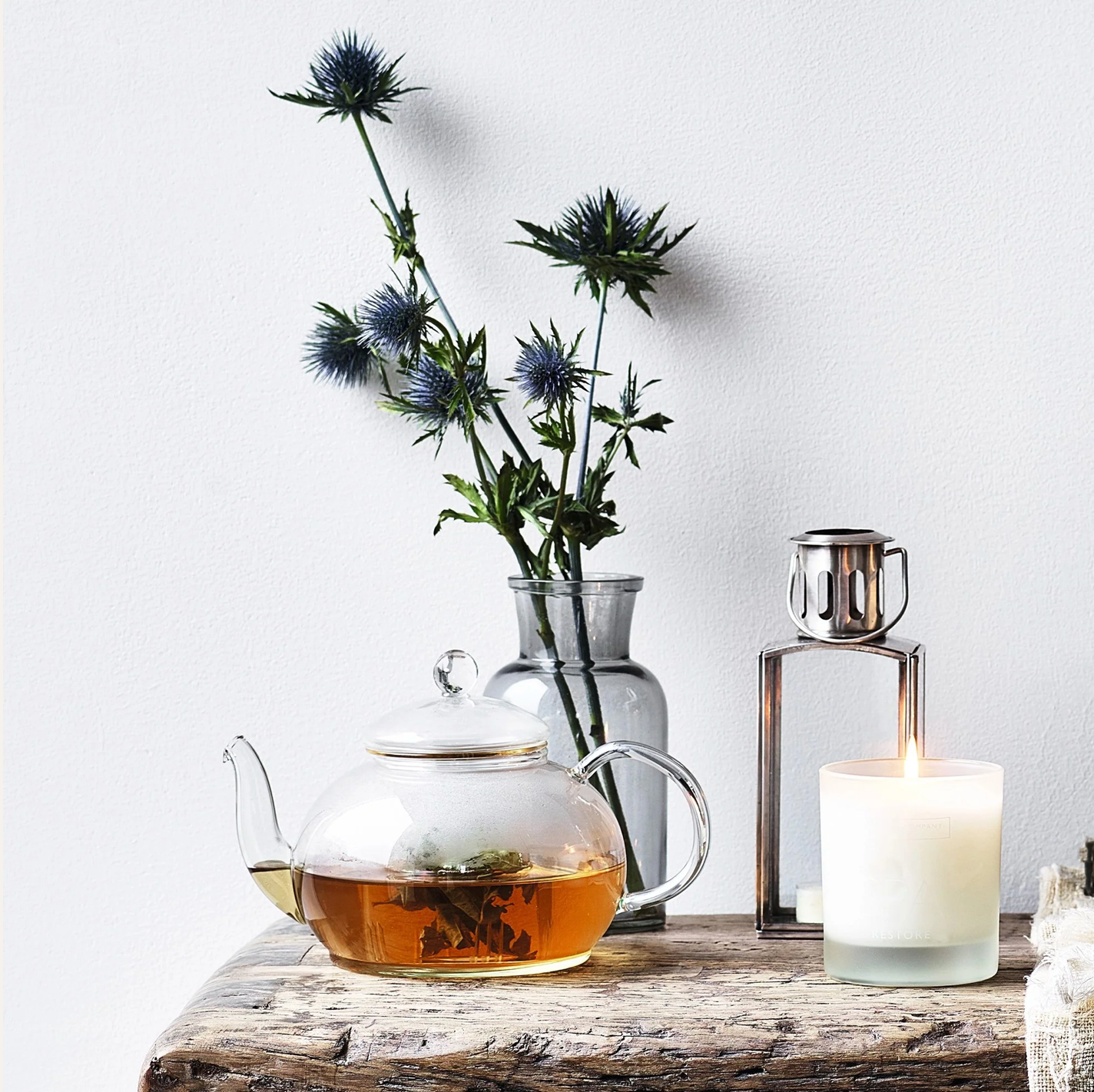 Tea set with teapot, candle, and vase with flowers on a wooden surface.