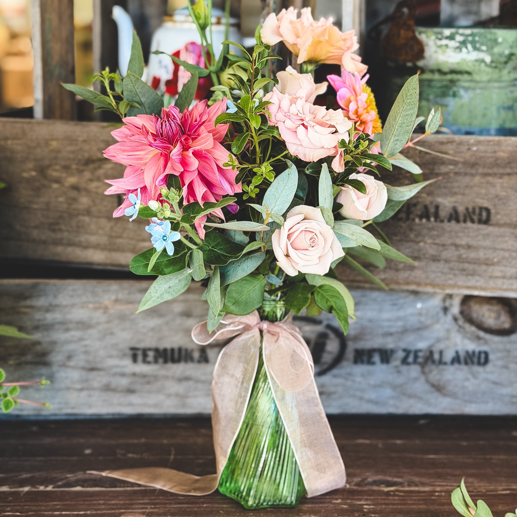 Bouquet of flowers with a green bud vase on a wooden surface, with a wooden crate in the background.