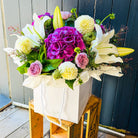 Bouquet of flowers in a white posy bag on a wooden crate against a wooden fence.