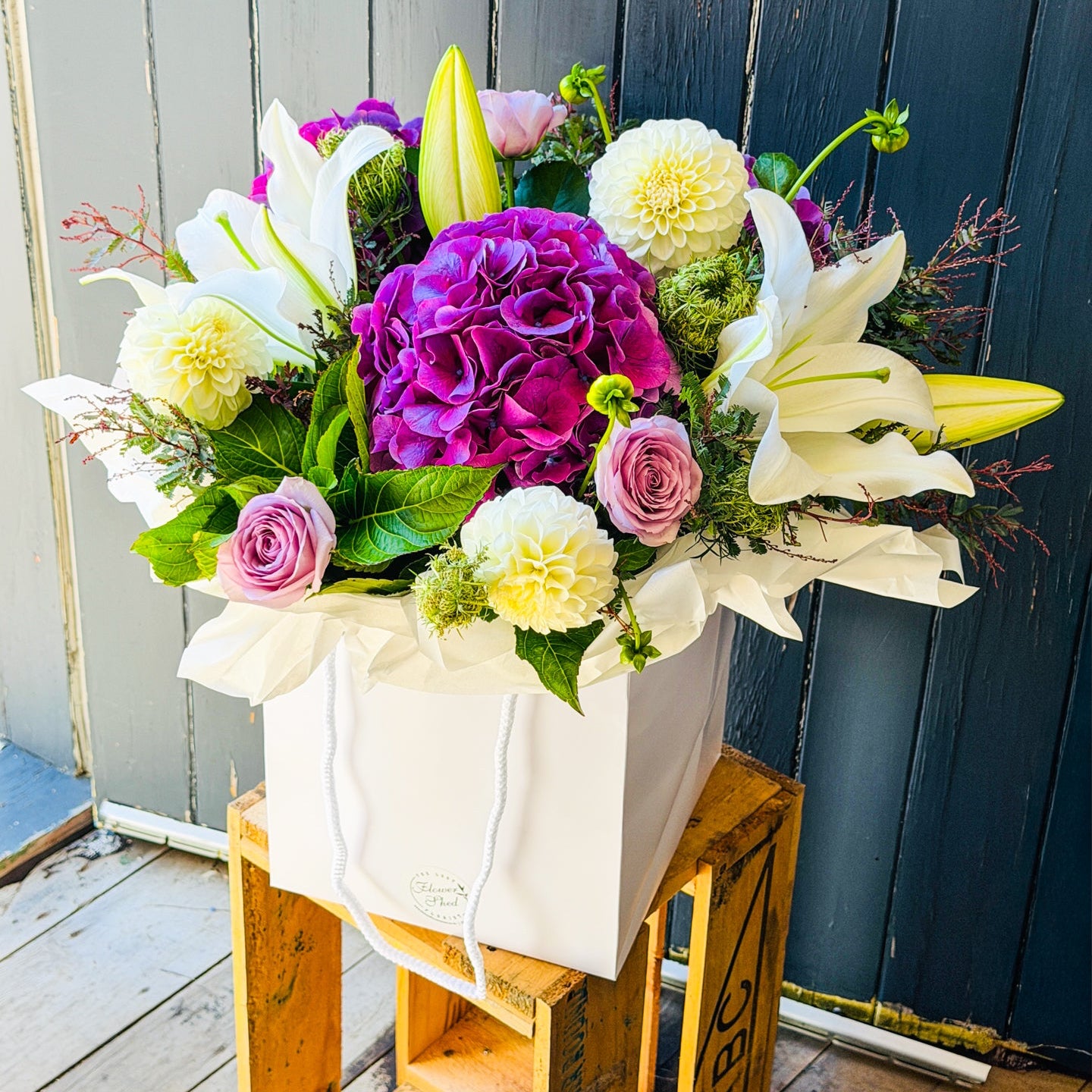 Bouquet of flowers in a white posy bag on a wooden crate against a wooden fence.