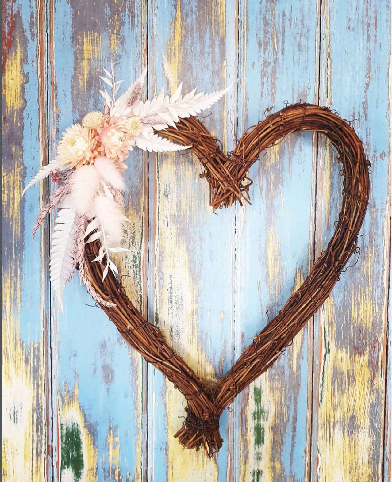 Heart-shaped wreath with feathers on a rustic wooden background