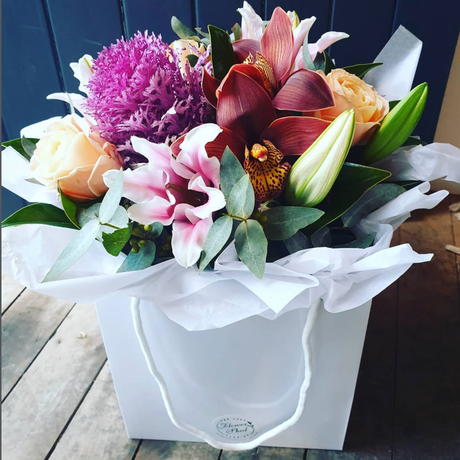 Bouquet of flowers in a white box on a wooden surface with a blue background