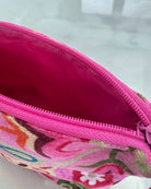 A close-up of a zippered pouch with a bright pink interior and a colorful floral patterned exterior, shown on a light reflective surface.