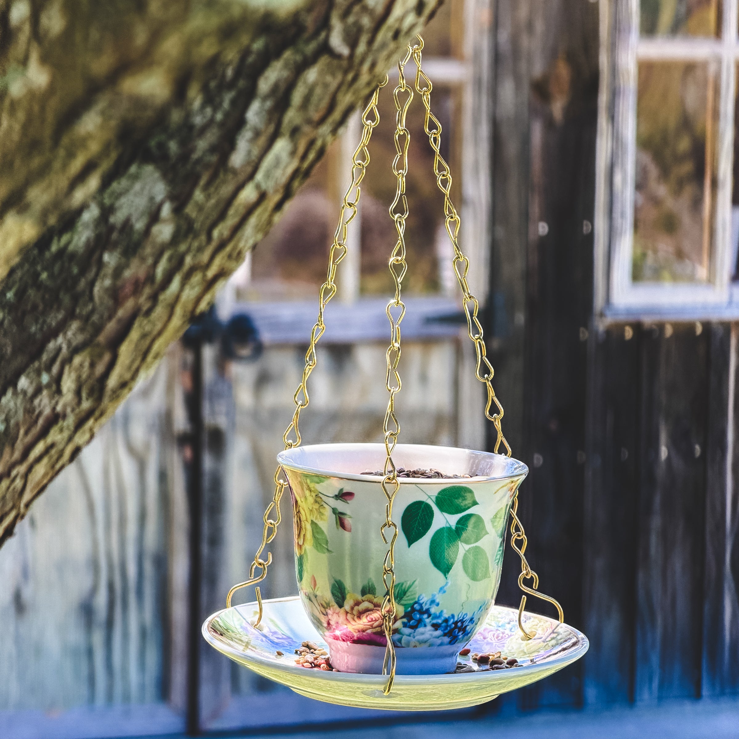 Decorative teacup and saucer bird feeder gift hanging from a chain against a blurred natural background