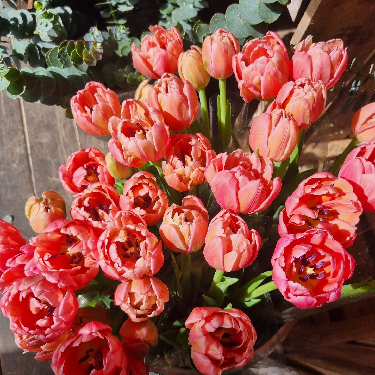 Bouquet of pink tulips with green leaves in a wooden box.