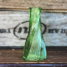 Bouquet of flowers with a green bud vase on a wooden surface, with a wooden crate in the background.