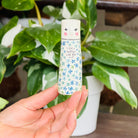 A tall cylindrical mini bud vase with floral design and text ' Life is better with you in it'.