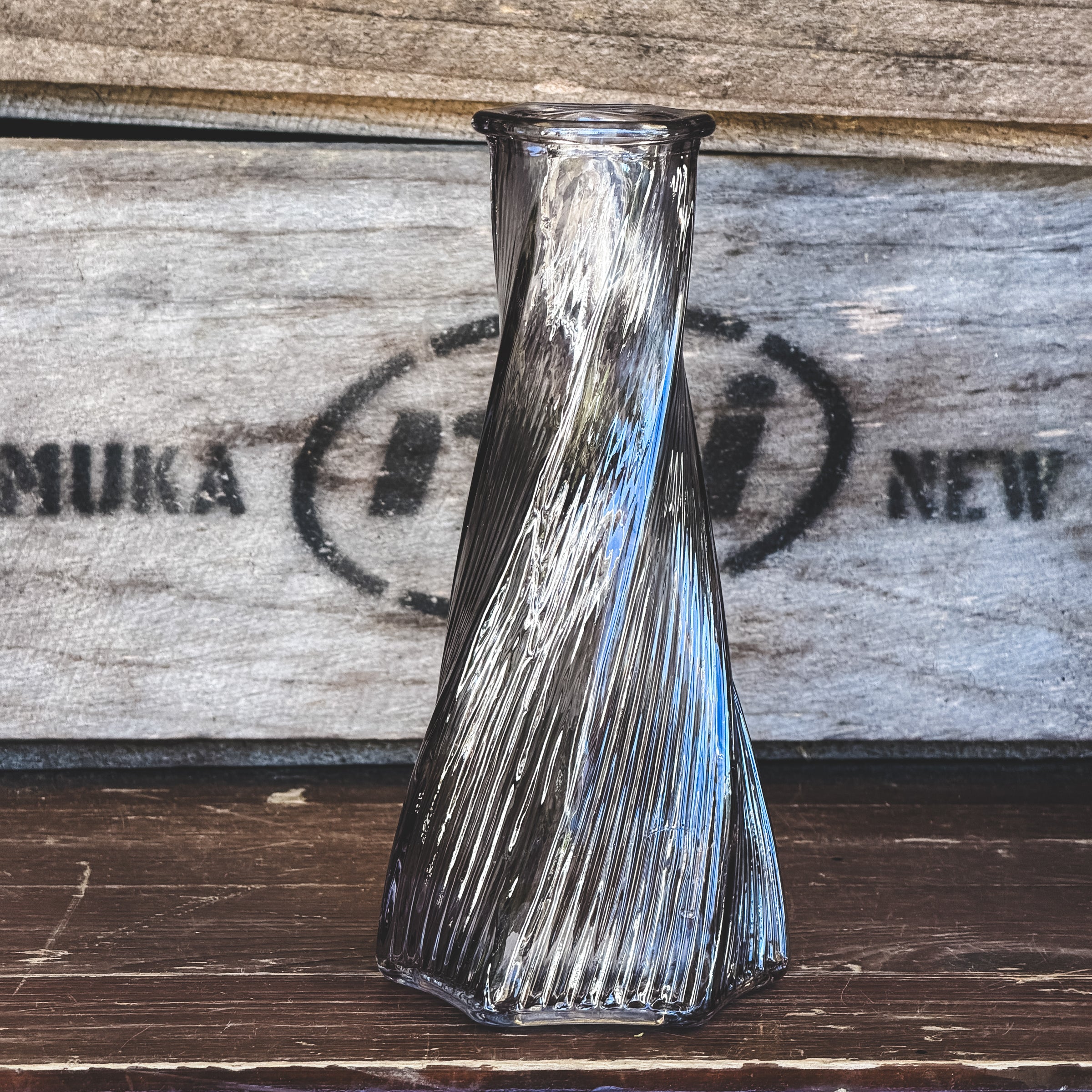 Bouquet of flowers with a green bud vase on a wooden surface, with a wooden crate in the background.