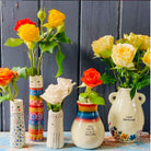 A tall cylindrical mini bud vase with floral design and text ' Life is better with you in it'.